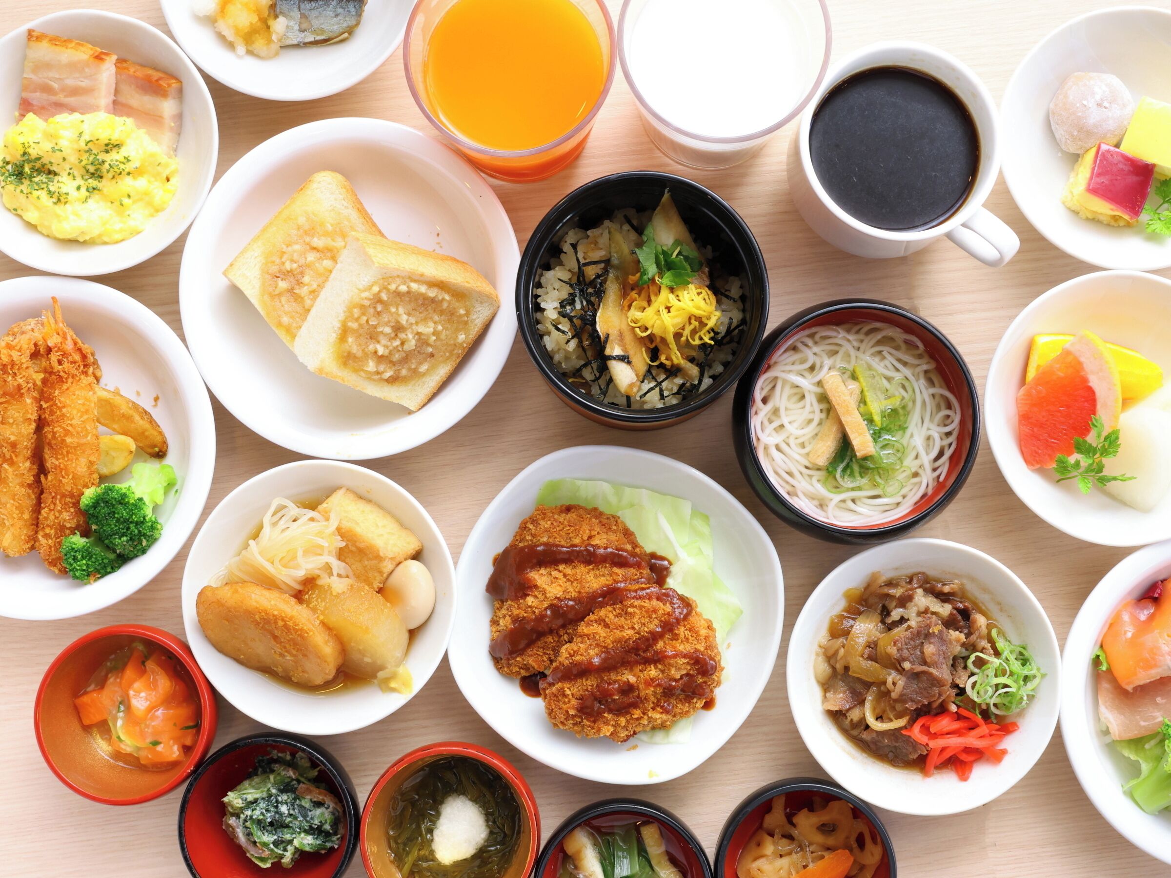 A variety of dishes arranged on a wooden table, including bread, noodles, and various side dishes.