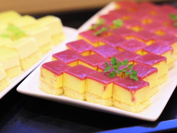 Un vassoio di dolci con torte a strati gialli e rosa, guarnito con una foglia di menta.