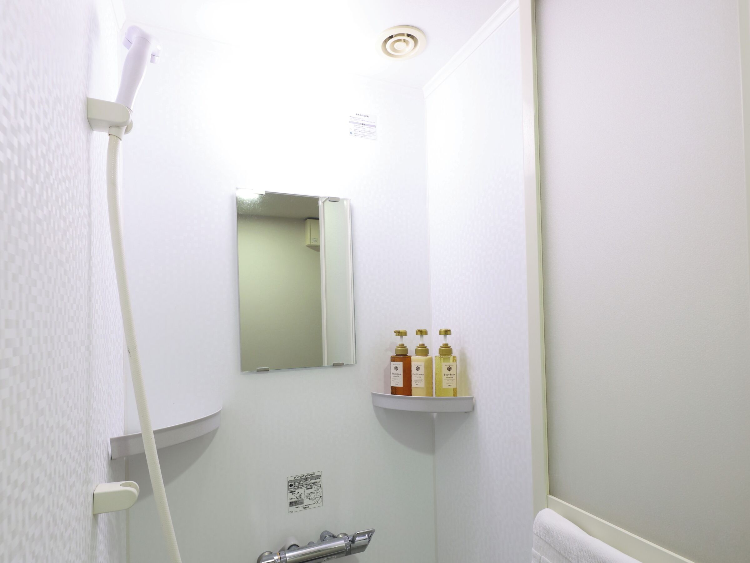 A bathroom with a white shower, a mirror, and a shelf with toiletries.