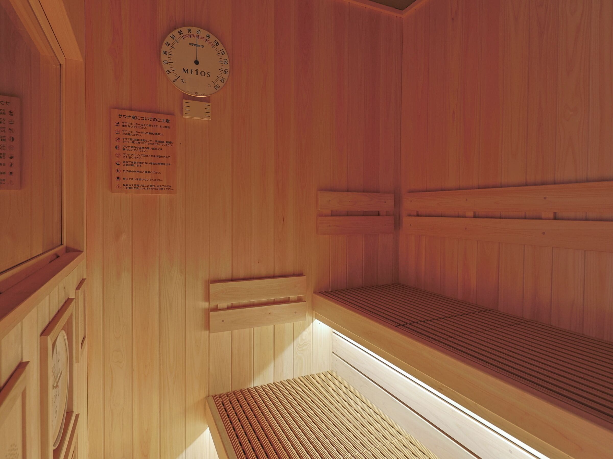 Una sauna con paredes de madera, un termómetro y un banco.