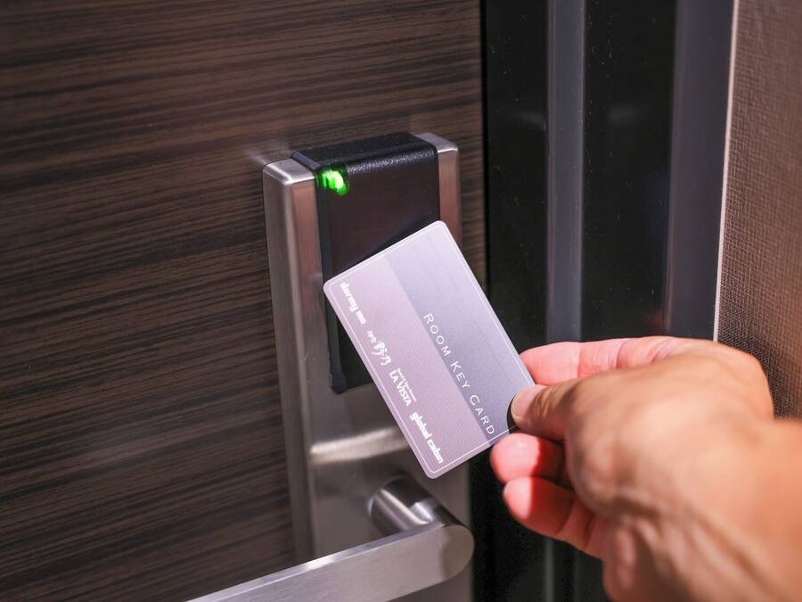 A hand holding a room key card near a door with a keypad and a green light indicator.