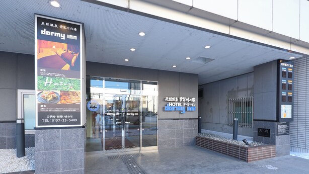 A modern hotel entrance with a glass door, a signboard advertising the hotel, and a tiled pavement.