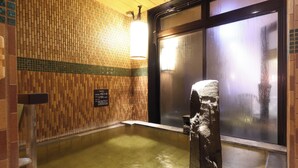 A traditional Japanese onsen with a wooden wall, a stone basin, and a glass door.