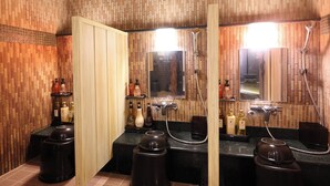 Un baño con paredes de paneles de madera, encimera negra y un espejo sobre el lavabo. Hay tres lavamanos, cada uno con su propio cabezal de ducha.