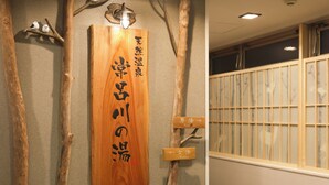 Un letrero de madera con caracteres japoneses, flanqueado por dos ramas, en un pasillo con una puerta corredera tradicional japonesa al fondo.