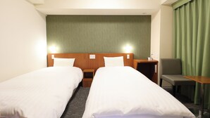 Habitación de hotel con dos camas individuales, cabecero de madera, cortina verde, sillón gris y una pequeña mesa.