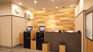 A reception area with a wooden wall, a clock, and two self-service kiosks.