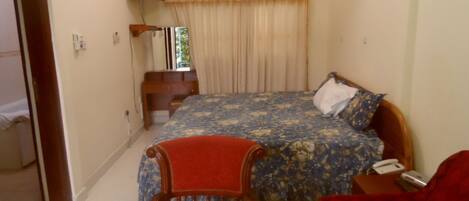A bedroom with a bed, a wooden chair, a red sofa, a desk, a television, and an air conditioning unit.