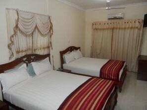A hotel room with two single beds, a wooden headboard, a bedside table, a nightstand, and a wall-mounted air conditioner. - De Holiday Beach Hotel (Kokrobite)