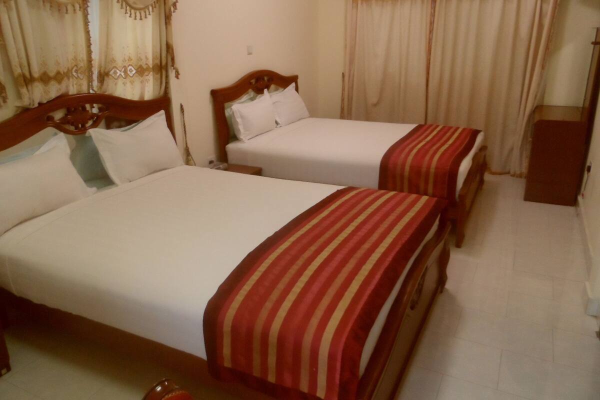 A hotel room with two single beds, a wooden headboard, a nightstand, and a small cabinet.