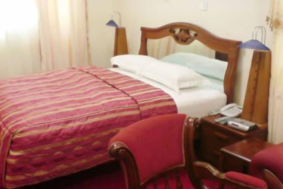 A hotel room with a bed, a chair, a nightstand, and a lamp.