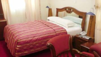 Una habitación de hotel con cama, una silla, una mesita de noche y una lámpara.