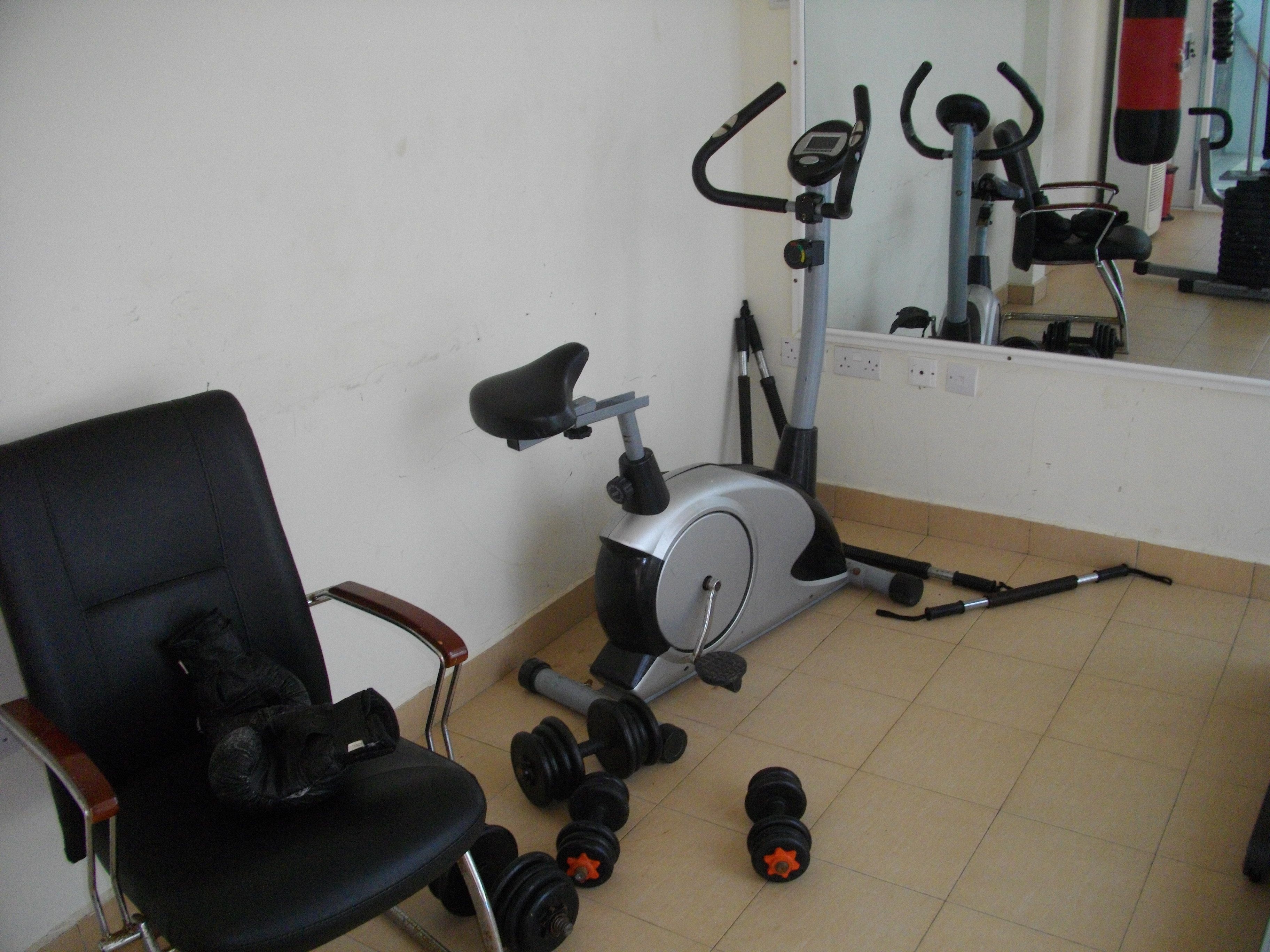 A home gym with an exercise bike, a stationary bike, and a chair with dumbbells.