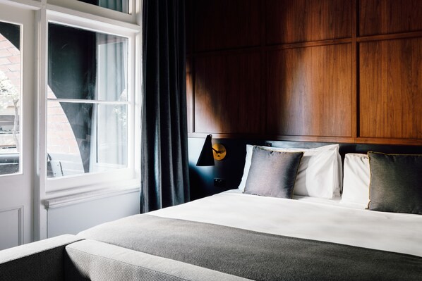 A bedroom with a large bed, a wooden headboard, a nightstand with a lamp, and a window with curtains.
