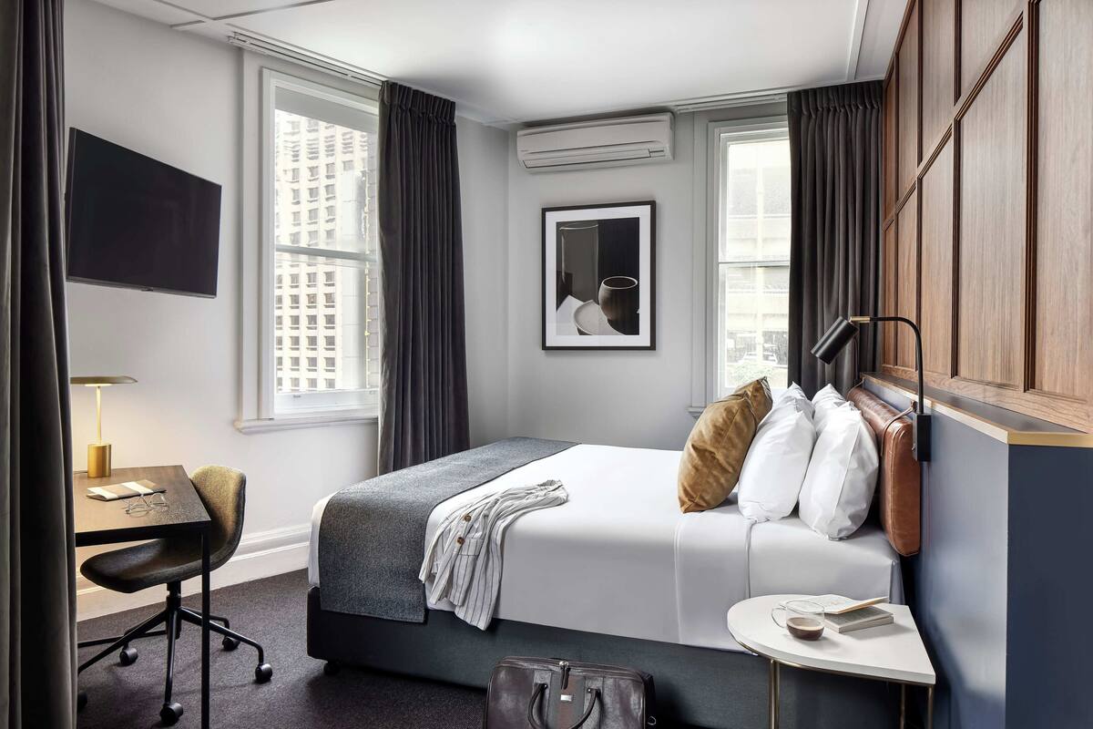 Une chambre d’hôtel avec un lit, un bureau, une chaise, une petite table, une valise et un téléviseur.