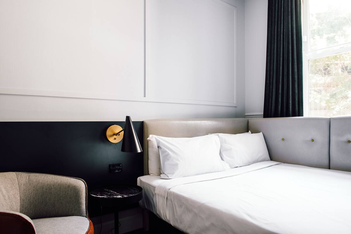 Une chambre d’hôtel avec un lit, une chaise, une petite table et une horloge murale.