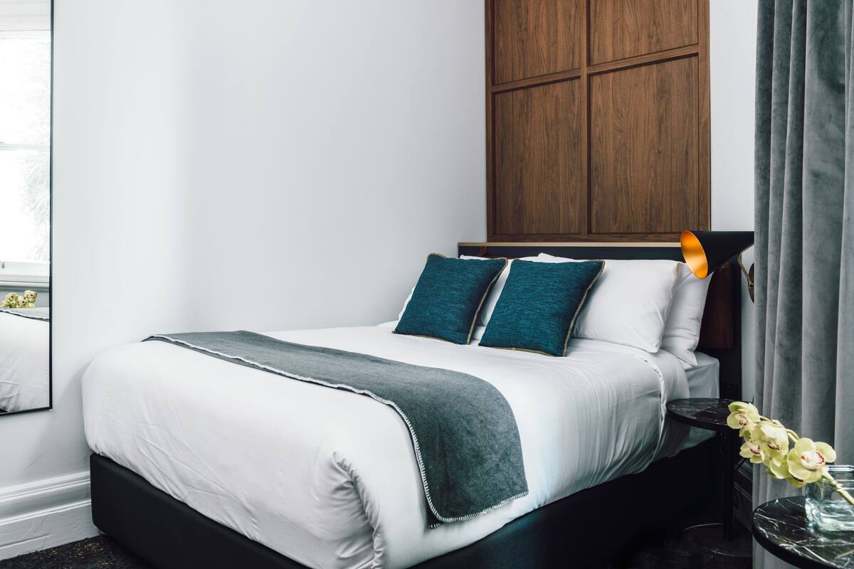 Un lit bien fait, avec une literie blanche et turquoise, une tête de lit sombre et un mur recouvert de panneaux en bois au-dessus.