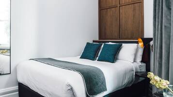 A neatly made bed with white and teal bedding, a dark headboard, and a wooden panel wall above.