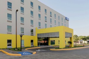 A modern hotel with a yellow entrance, a handicapped parking space, and a sign for City Express by Marriott.