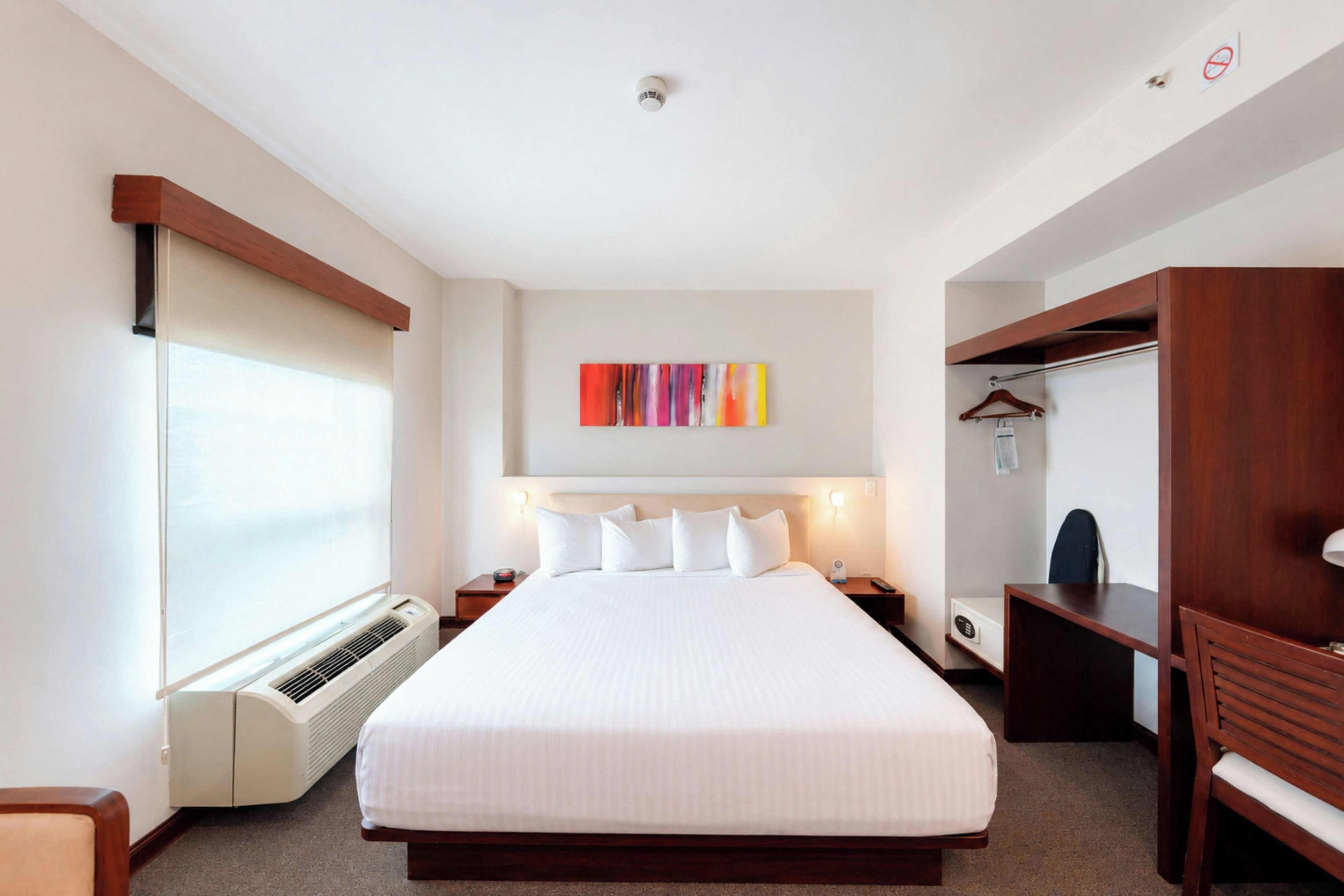 A hotel room with a large bed, bedside tables, a wardrobe, a heater, and a wall-mounted artwork.