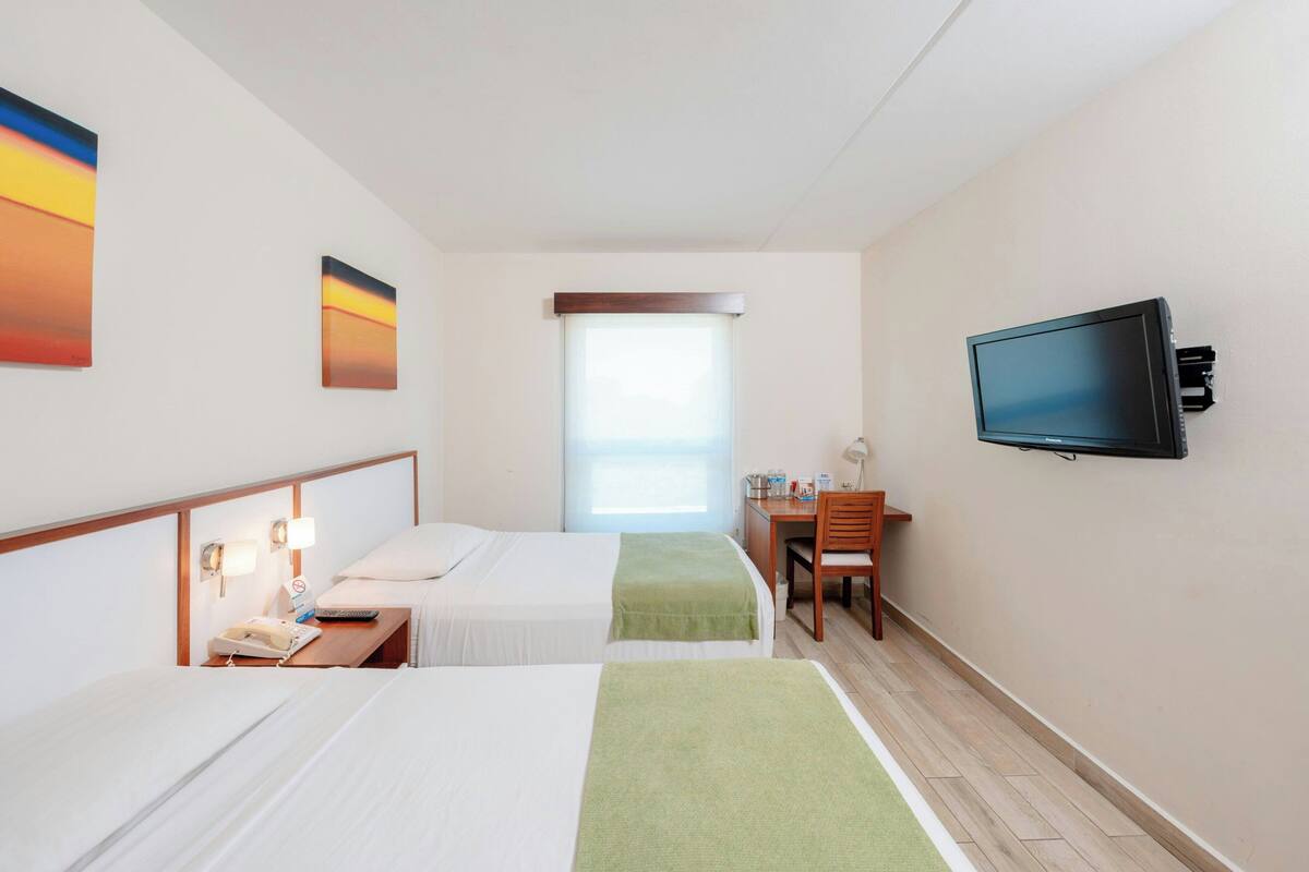 Une chambre d’hôtel avec deux lits, un bureau, une télévision et une fenêtre.