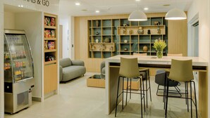 A modern kitchen with a 'GRAB & GO' snack machine, a dining area with bar stools, and a variety of decorative items on shelves. - City Express by Marriott Managua (Managua)