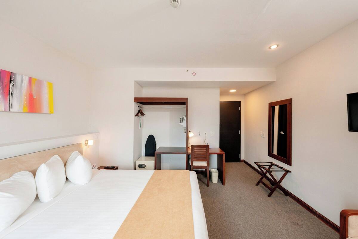 Une chambre d’hôtel avec un lit, un bureau, une chaise, une télévision et un tableau au mur.