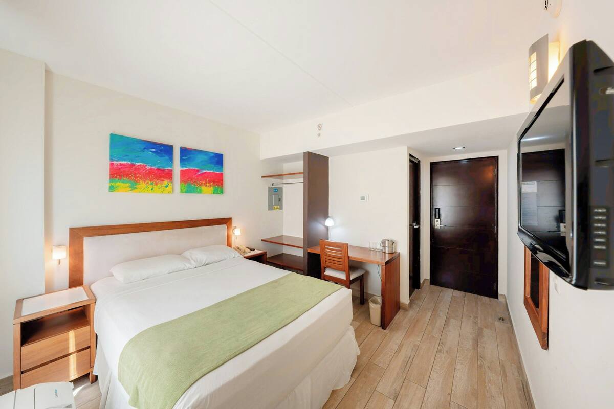 Une chambre d’hôtel comprenant un lit, un bureau, une chaise, une télévision, des œuvres d’art et une porte.