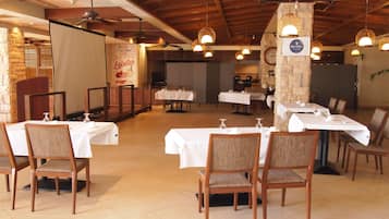 Un restaurant doté de nombreuses tables et chaises, de poutres en bois au plafond, de murs en pierre et de luminaires suspendus.