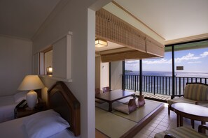 A hotel room with a balcony overlooking the sea, a bed with a bedside table and lamp, and a seating area with a table and chairs. - Guam Reef Hotel (Tamuning)