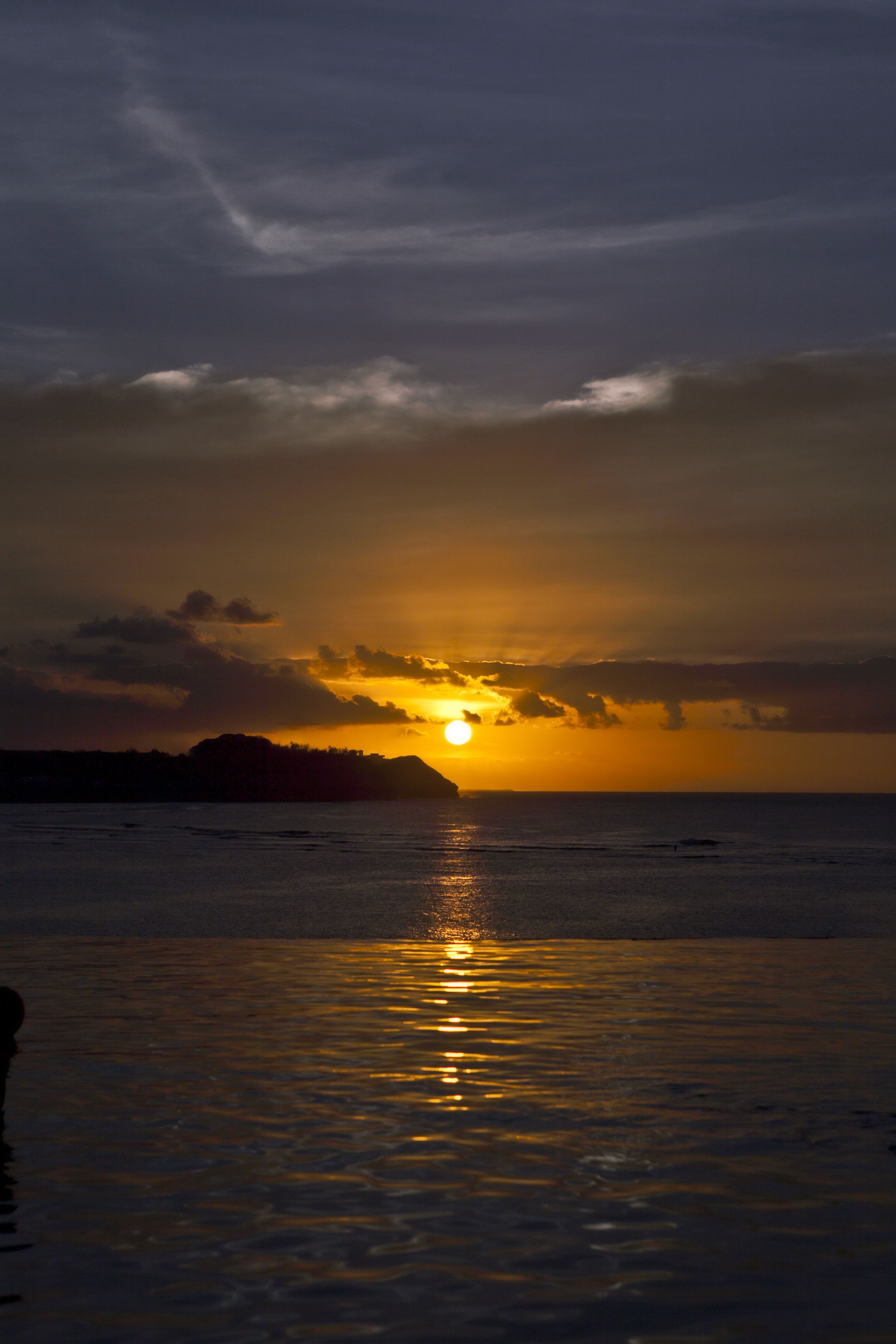 A sunset over a calm sea with a silhouette of land in the distance.