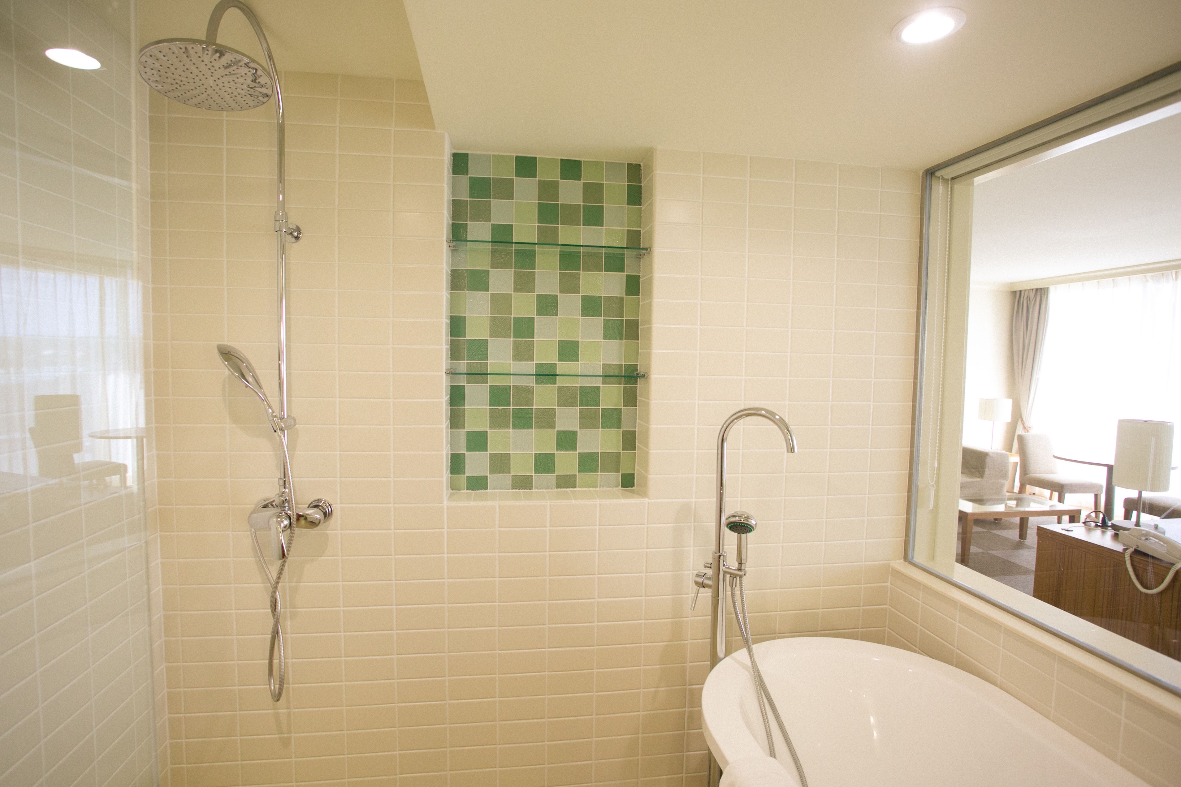 A bathroom with a bathtub, a shower, and a tiled wall with a green mosaic.