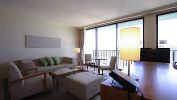 A hotel room with a sofa, chairs, a small table, a desk with a lamp, and large windows offering a city view.