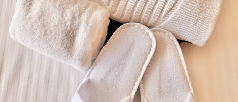 A pair of white slippers and a rolled-up white towel on a striped fabric surface.
