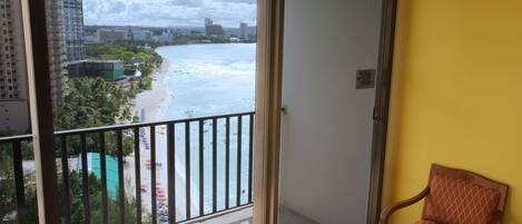 A balcony with a view of a beach and ocean, a chair, and a yellow wall.