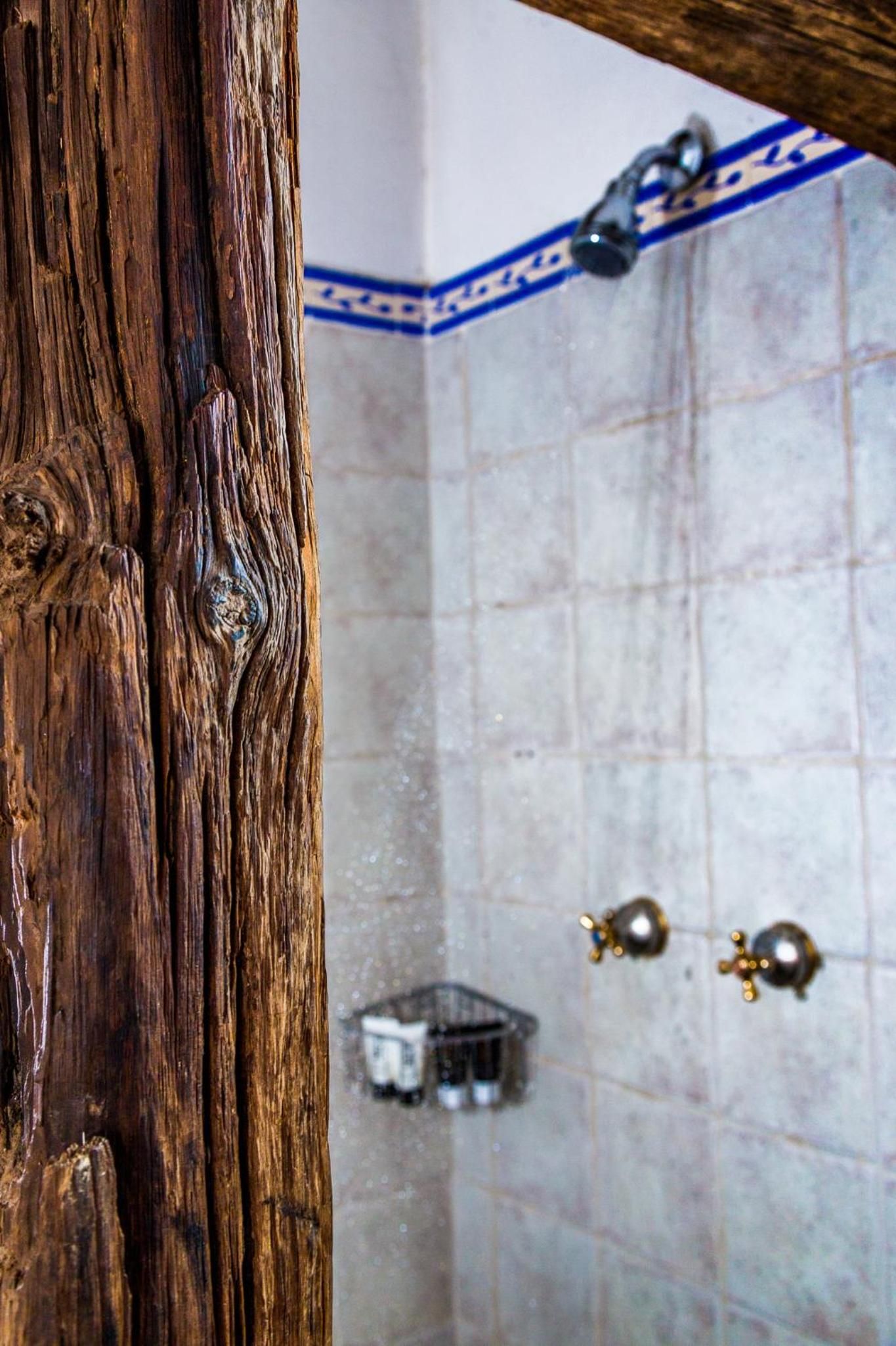 A wooden door frame and a tiled shower area with a showerhead and a small shelf.