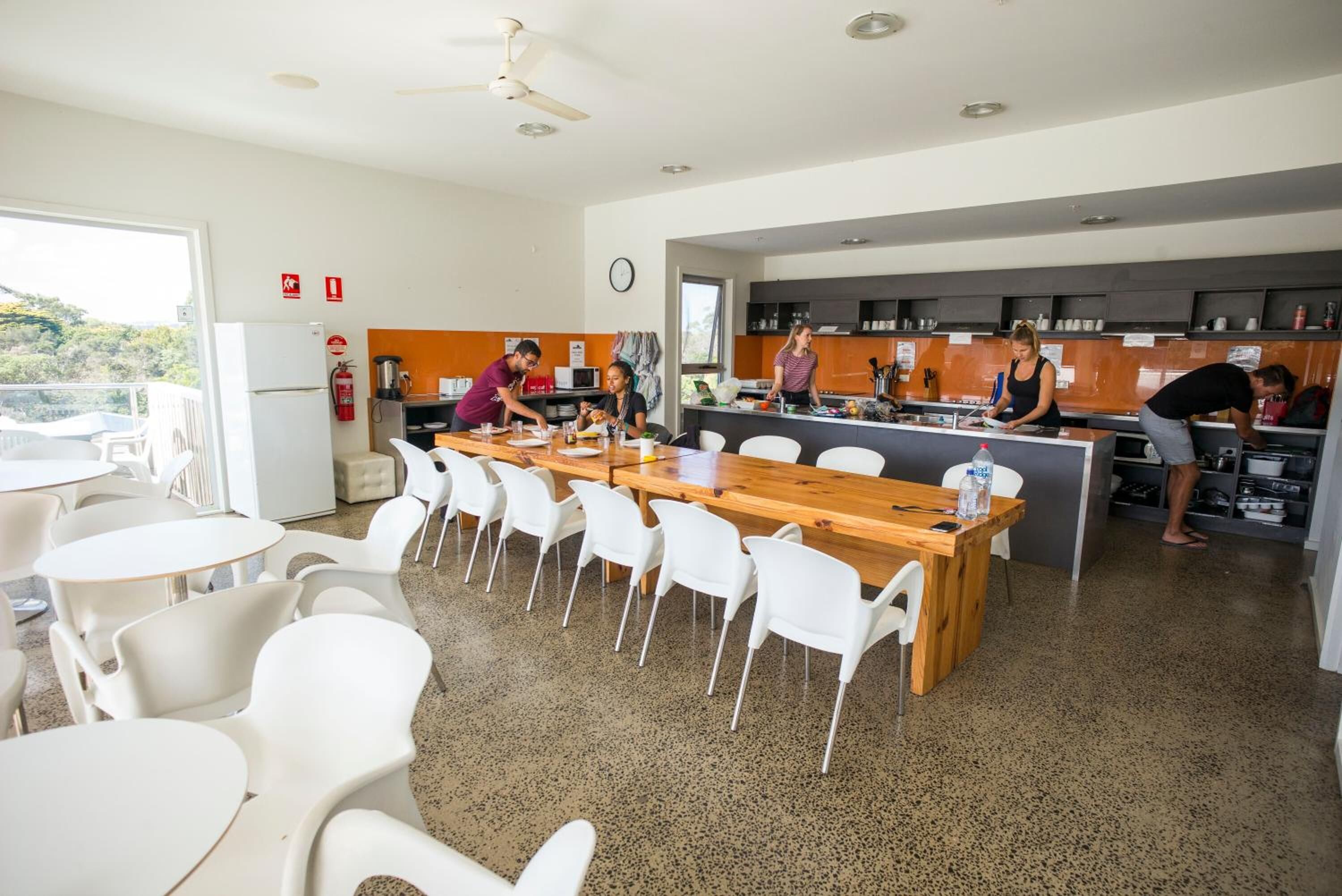 Una cucina moderna con sedie bianche e un tavolo di legno, un estintore e una sveglia appesa al muro.