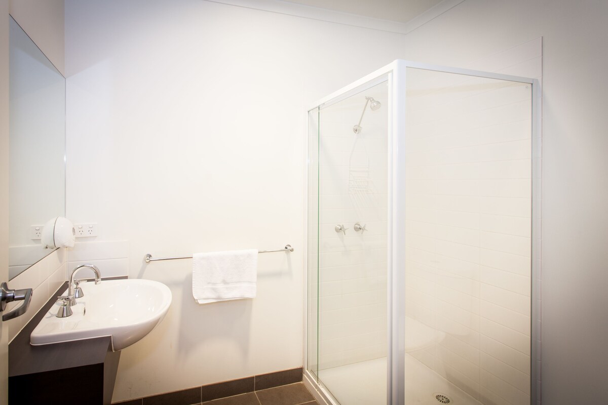 A modern bathroom with a glass shower enclosure, a white sink, and a towel rack.