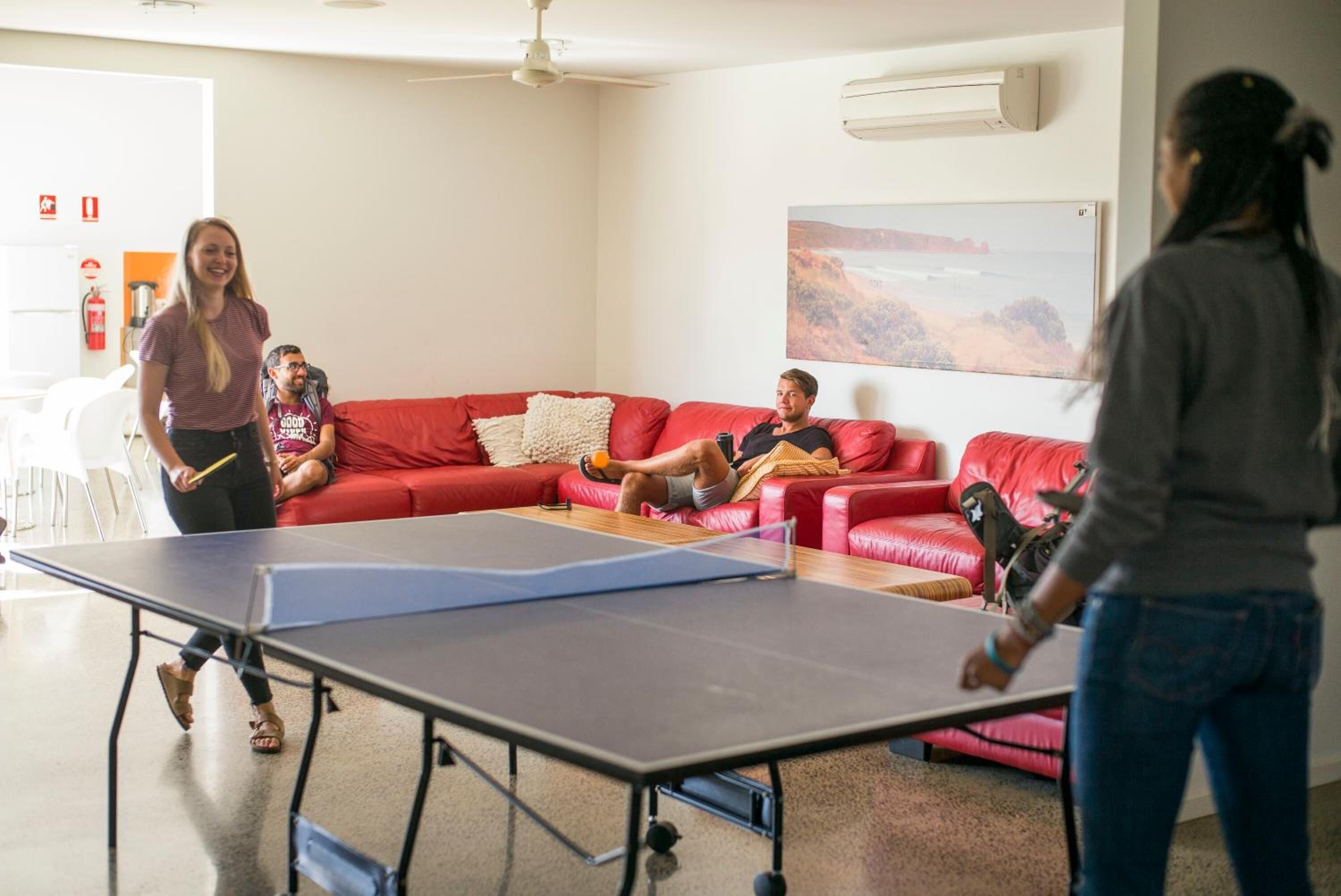 A room with a ping pong table, red leather couches, and a painting on the wall.