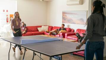 A room with a ping pong table, red leather couches, and a painting on the wall.