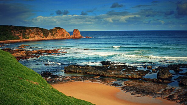 A coastal landscape with rocky shores, a sandy beach, and a prominent rock formation in the distance. - The Island Accommodation (Newhaven)
