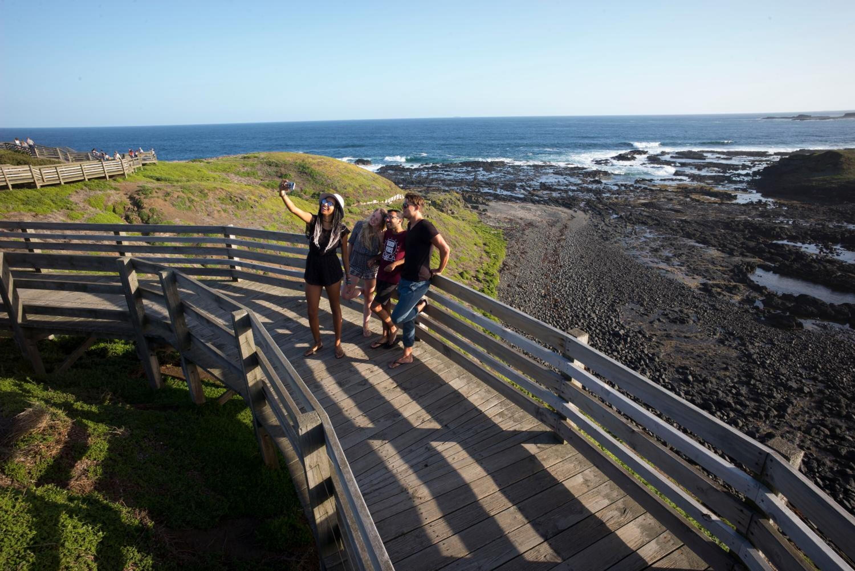 A wooden boardwalk with a railing, leading to a rocky shoreline with the ocean in the background.