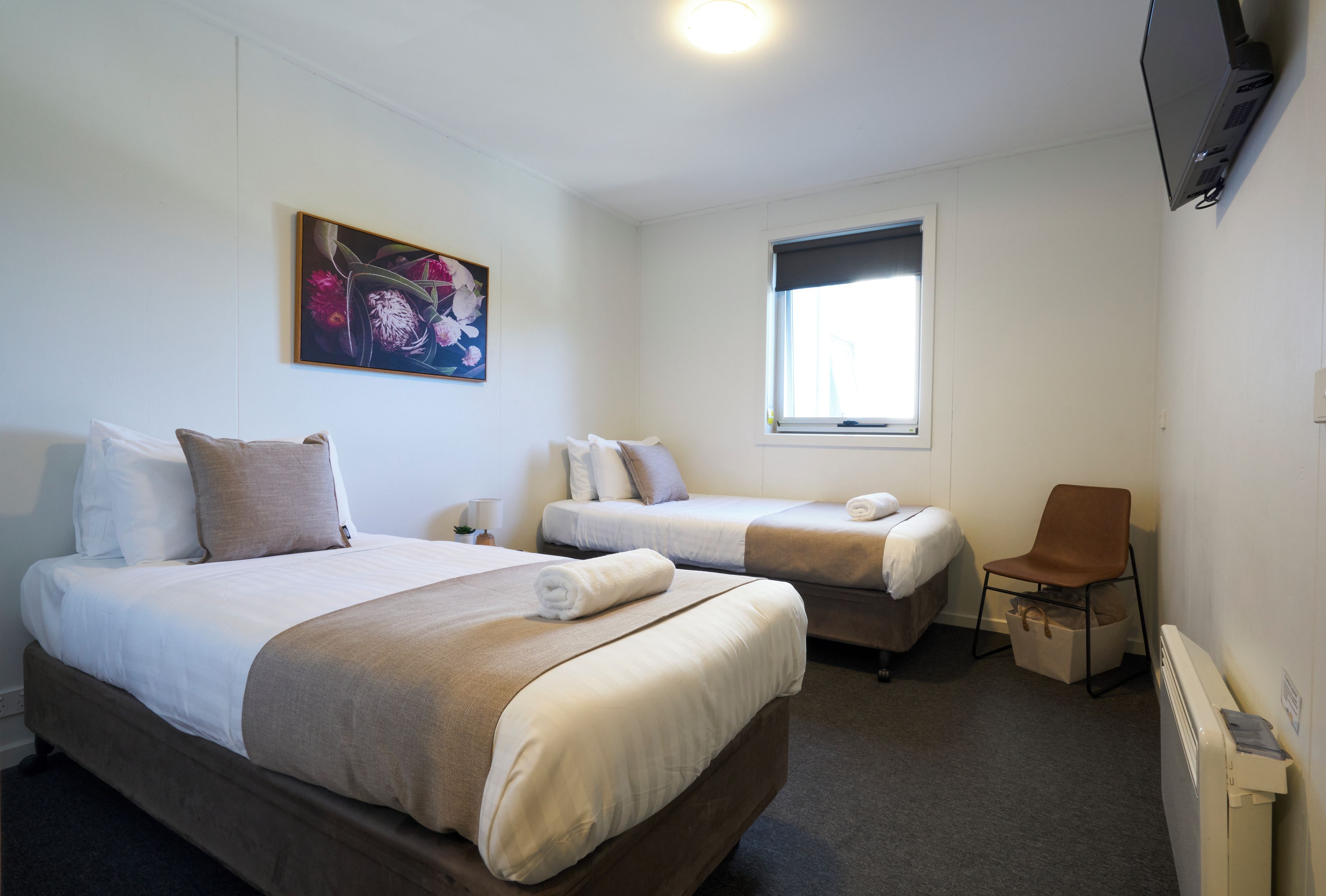A hotel room with two beds, a window, a painting, and a TV.