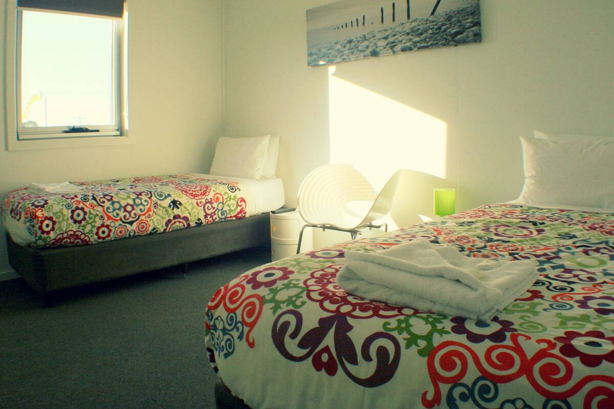 A hotel room with two beds, a chair, and a window.
