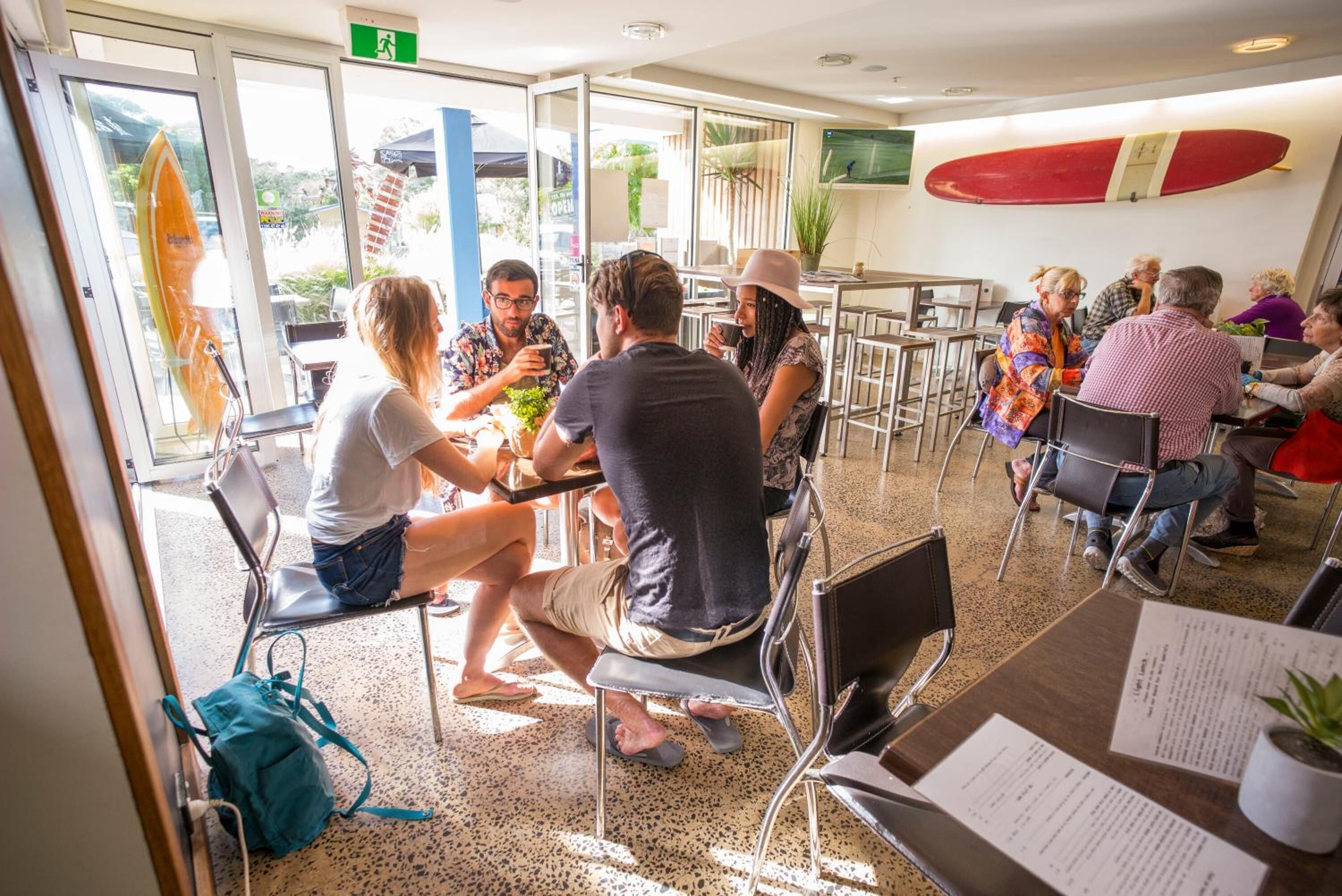 A group of people seated at tables in a well-lit indoor dining area with a surfboard on the wall.