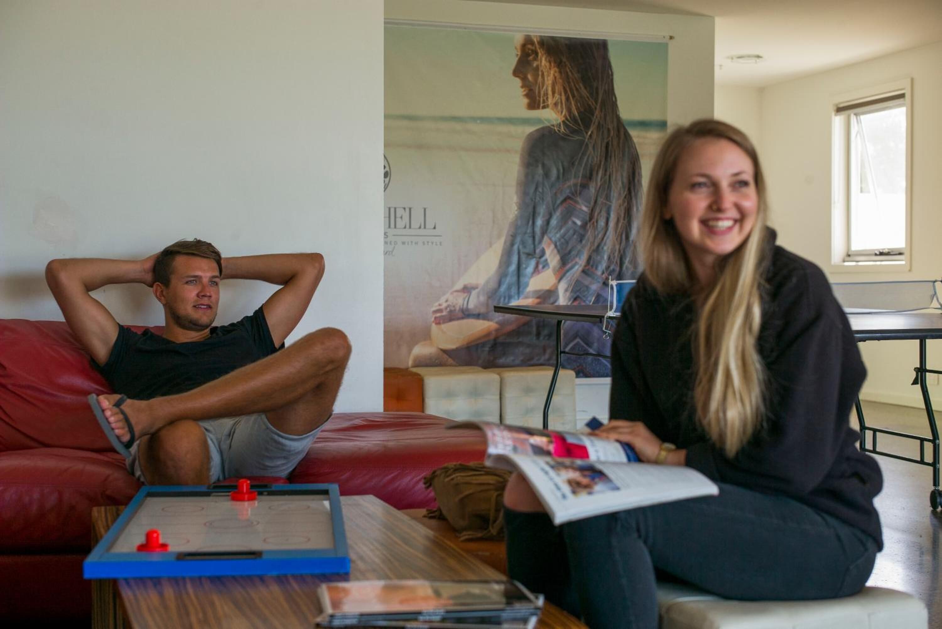 A living room with a red couch, a coffee table with a foosball table, and a poster on the wall.