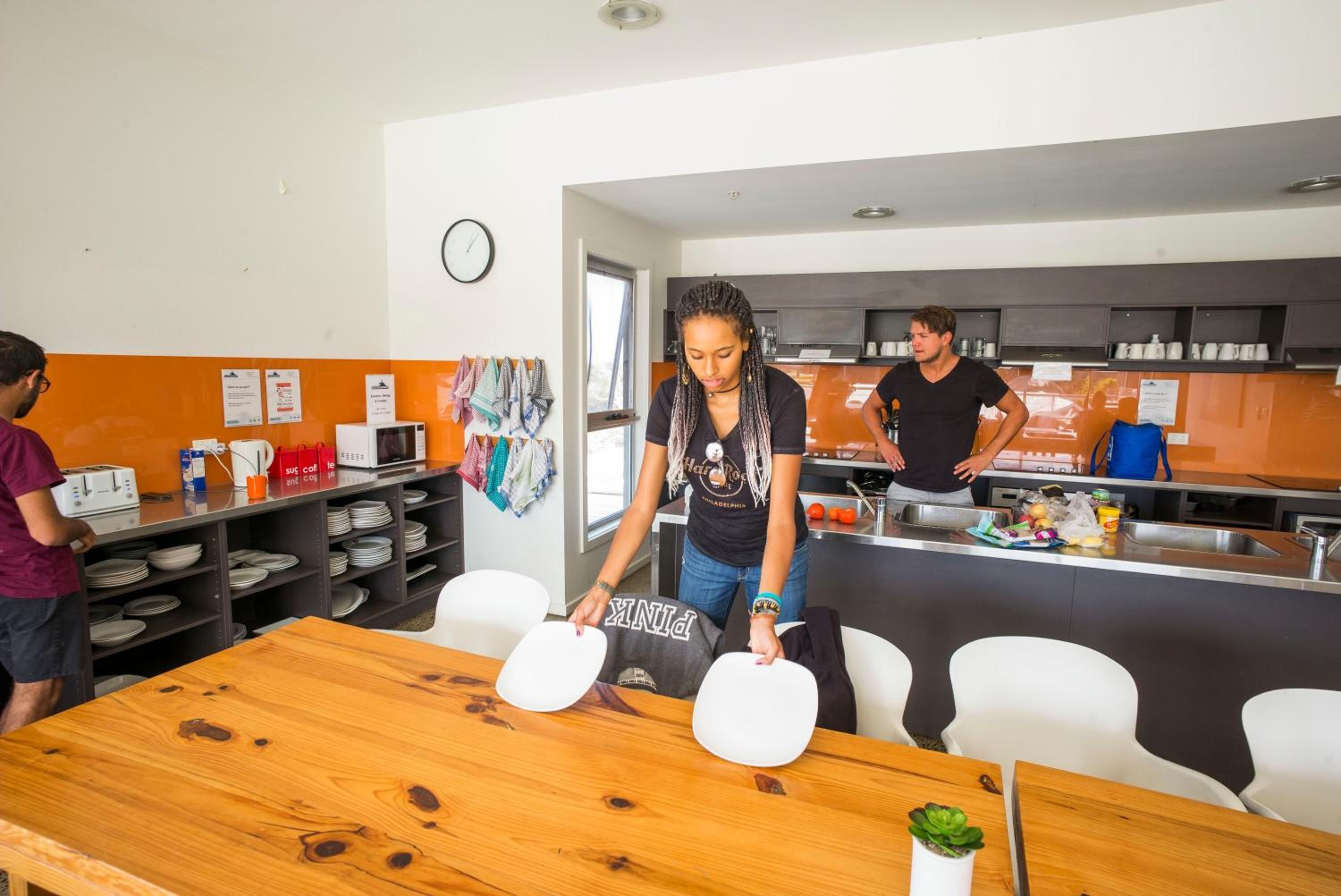Een moderne keuken met een houten tafel, witte stoelen en iemand die kookt.