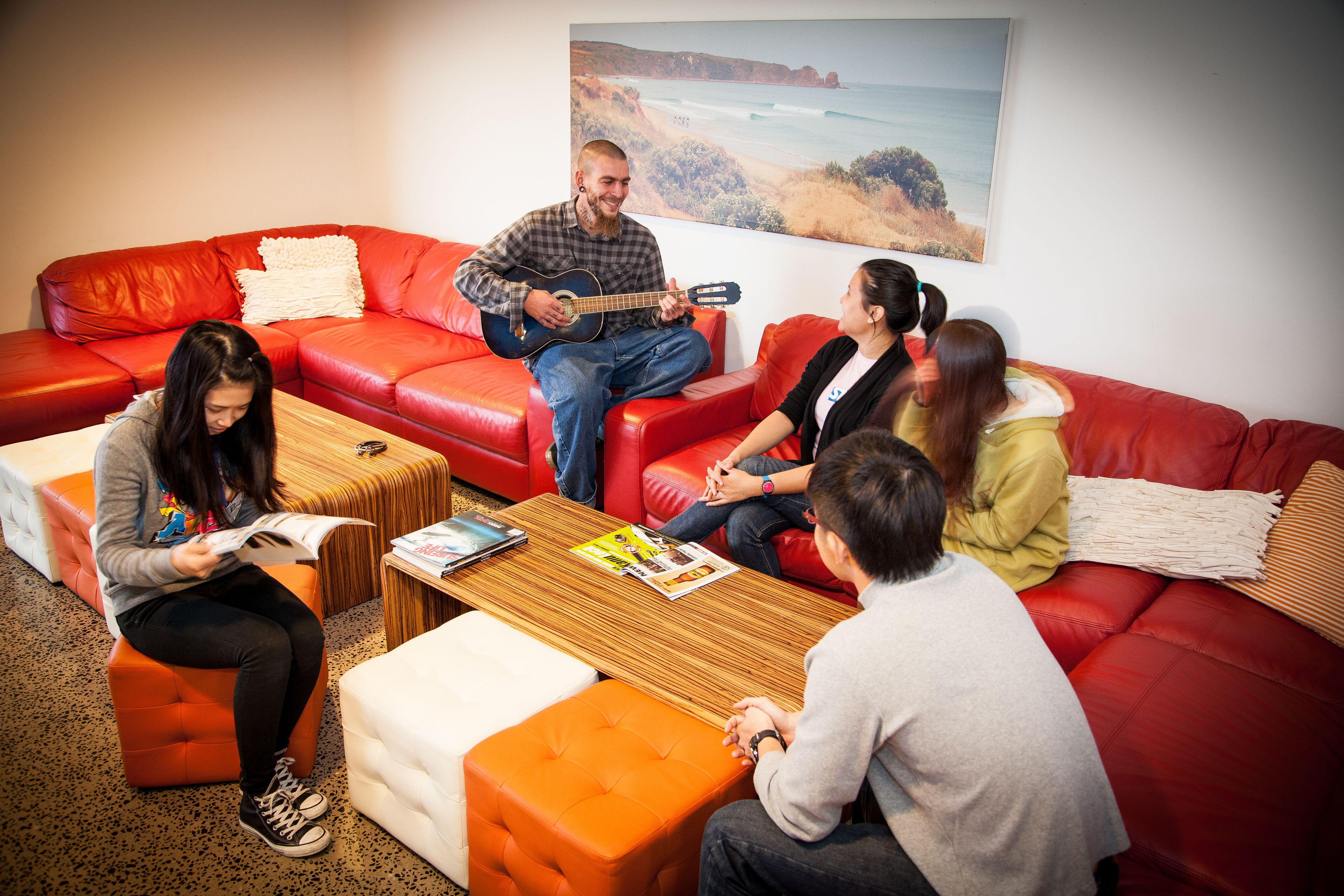 A group of people sitting on red leather couches in a modern living room with a wooden coffee table and a large landscape painting on the wall.