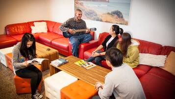 Un grupo de personas sentadas en sofás de cuero rojo en una sala de estar moderna con una mesa de centro de madera y un cuadro grande de un paisaje en la pared.