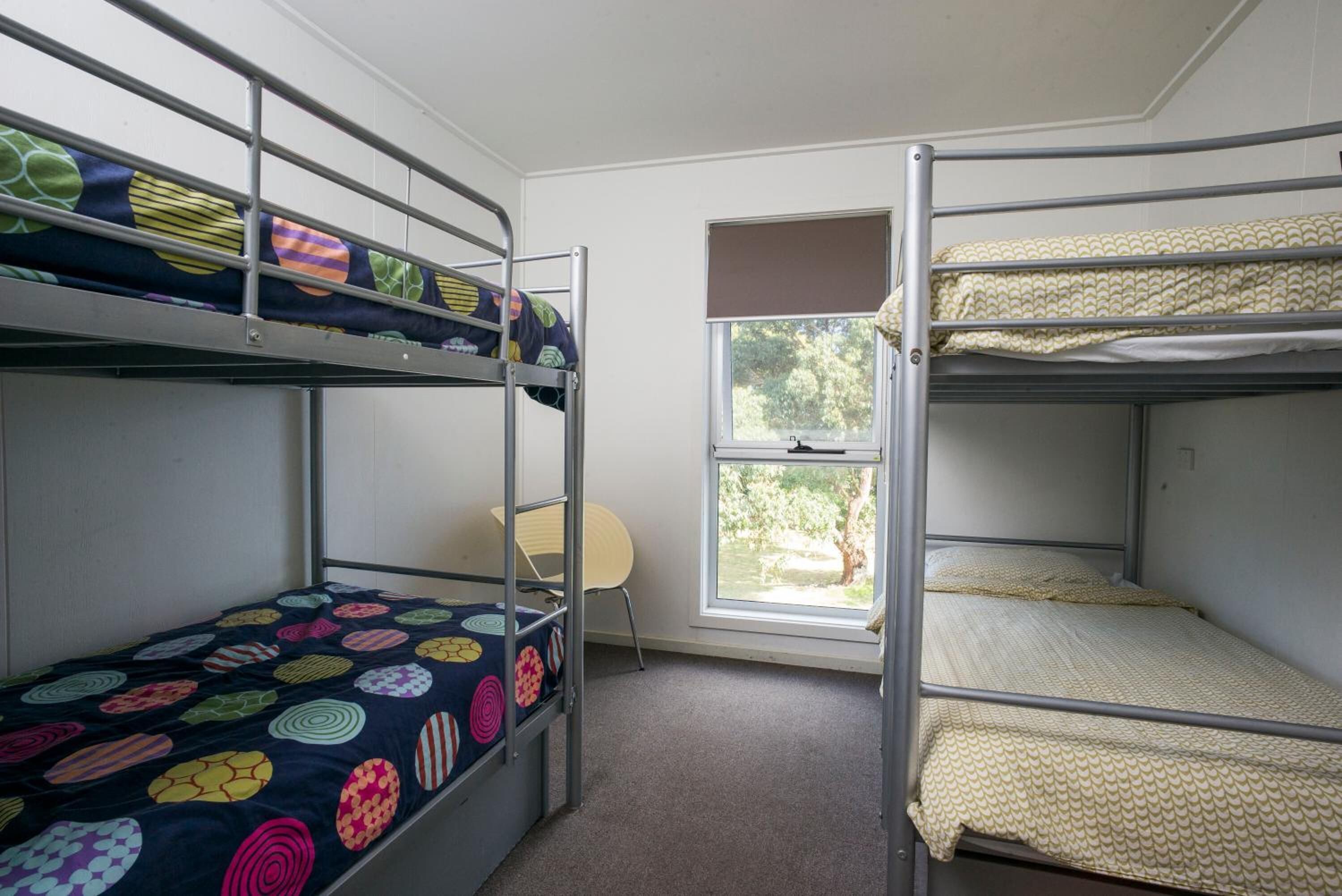 Une chambre de dortoir avec des lits superposés, une fenêtre donnant sur les arbres et une chaise.